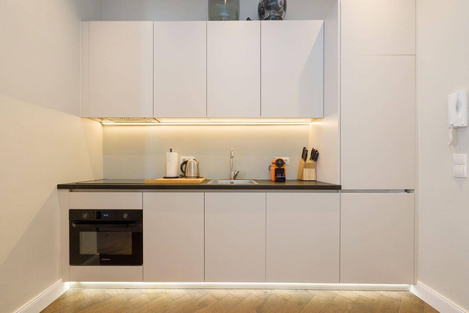 Kompakte Küchenzeile mit minimalistischem Design, Unterbauleuchten und modernen Geräten.