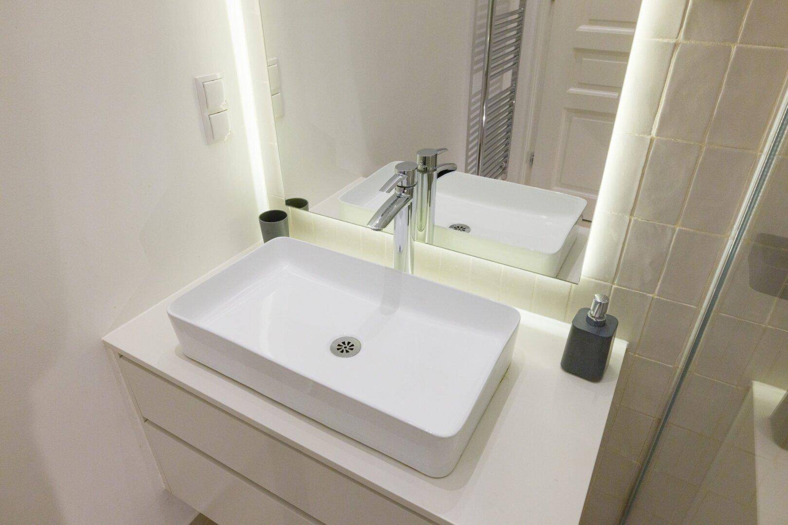 Moderner Waschtisch mit Aufsatzwaschbecken und beleuchtetem Spiegel im Badezimmer.