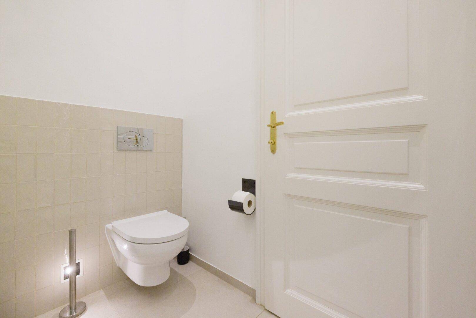 Separates WC mit wandhängender Toilette und hellen Fliesen.