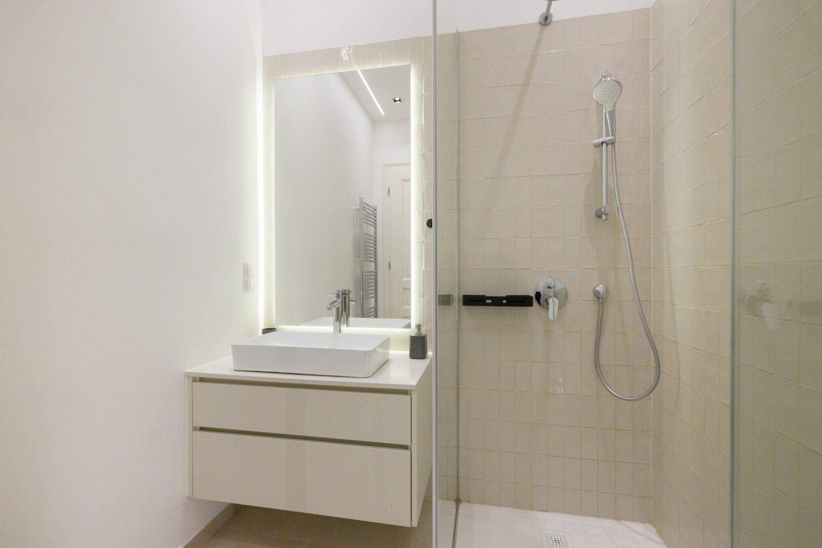 Modernes Badezimmer mit stilvollem Waschtisch, beleuchtetem Spiegel und begehbarer Dusche.