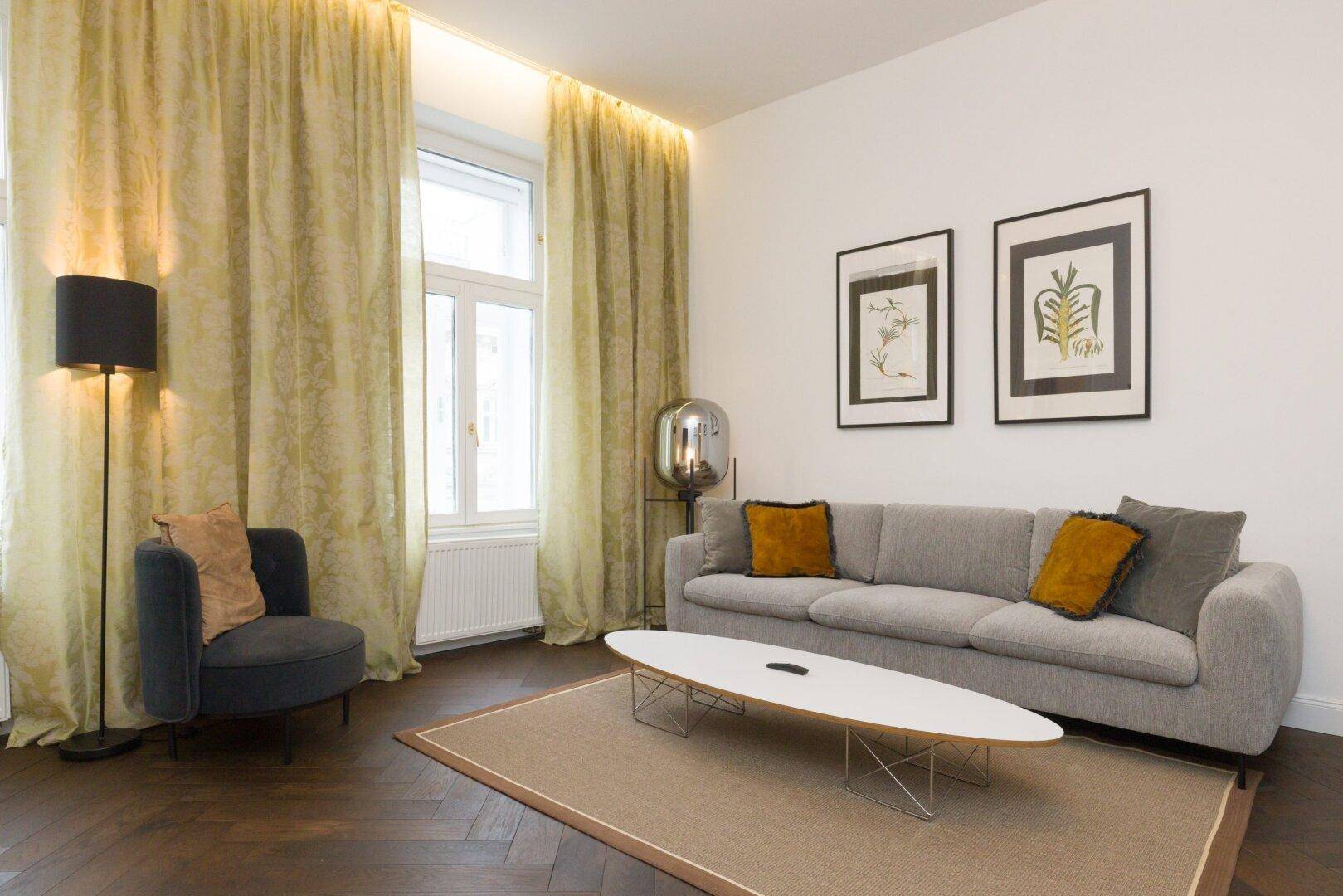Gemütlicher Wohnbereich mit Sofa, Sessel und dekorativen Bildern an der hellen Wand.