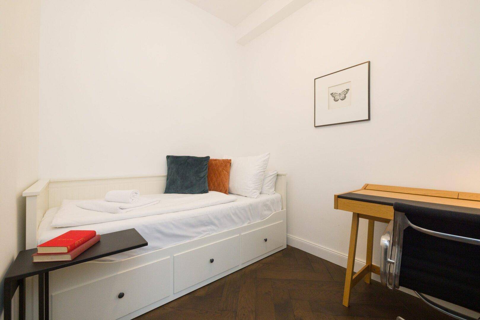 Kleines Schlafzimmer mit Einzelbett, Schreibtisch und minimalistischer Dekoration.
