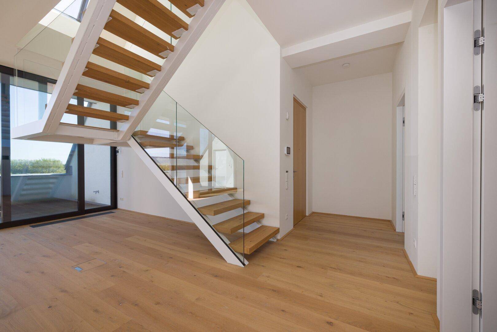 Moderne Holztreppe mit Glasgeländer, die verschiedene Ebenen des Hauses verbindet.