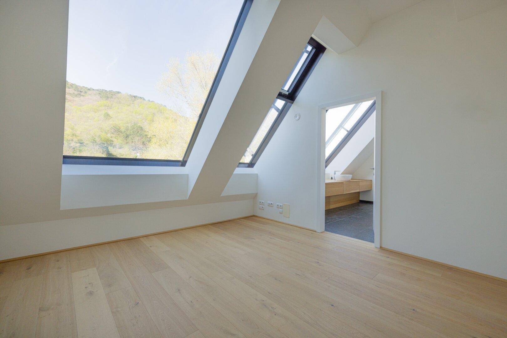 Helles Schlafzimmer im Dachgeschoss mit Holzboden und Zugang zu einem modernen Bad.