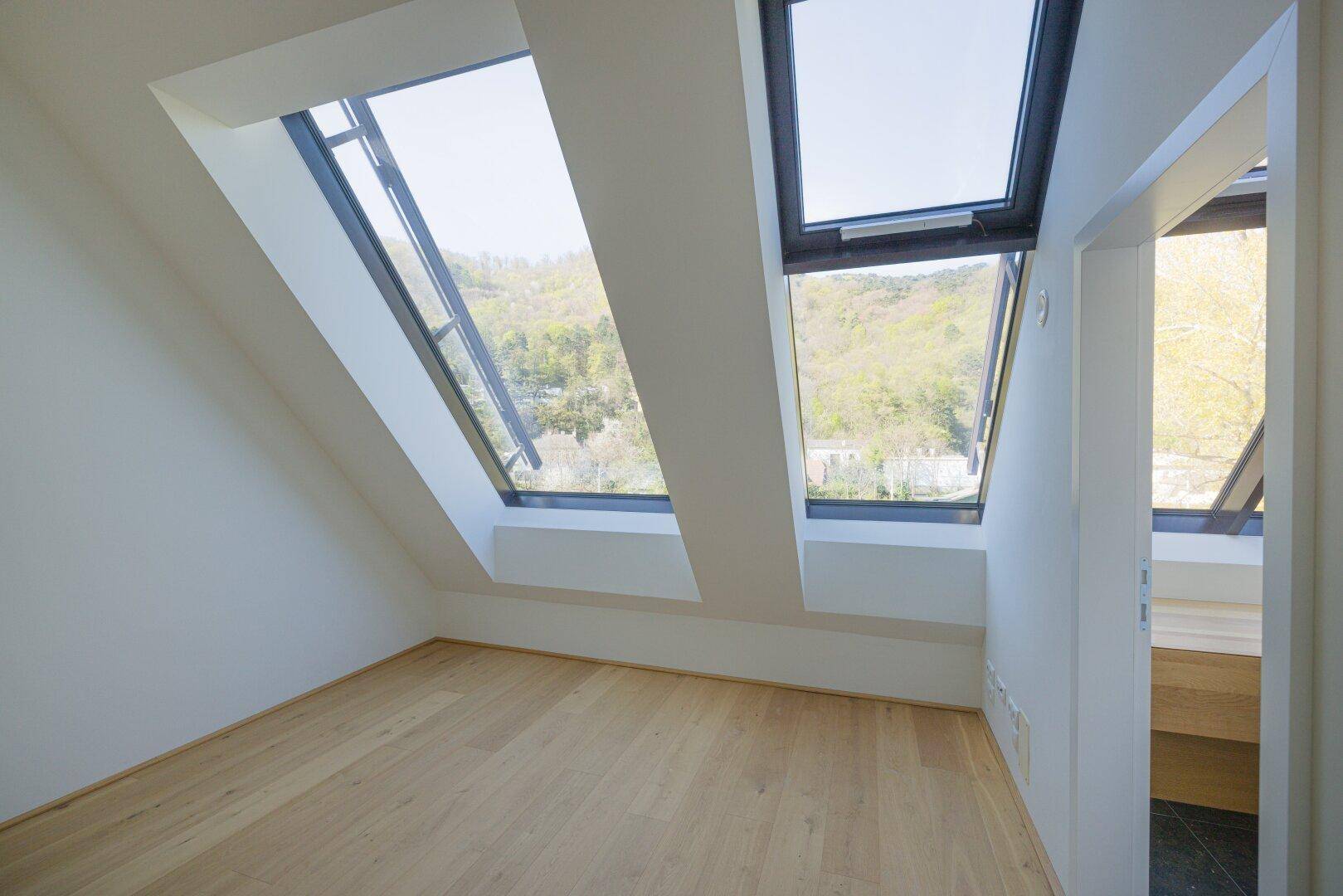 Schlafzimmer mit schrägen Wänden, Holzboden und zwei großen Dachfenstern.