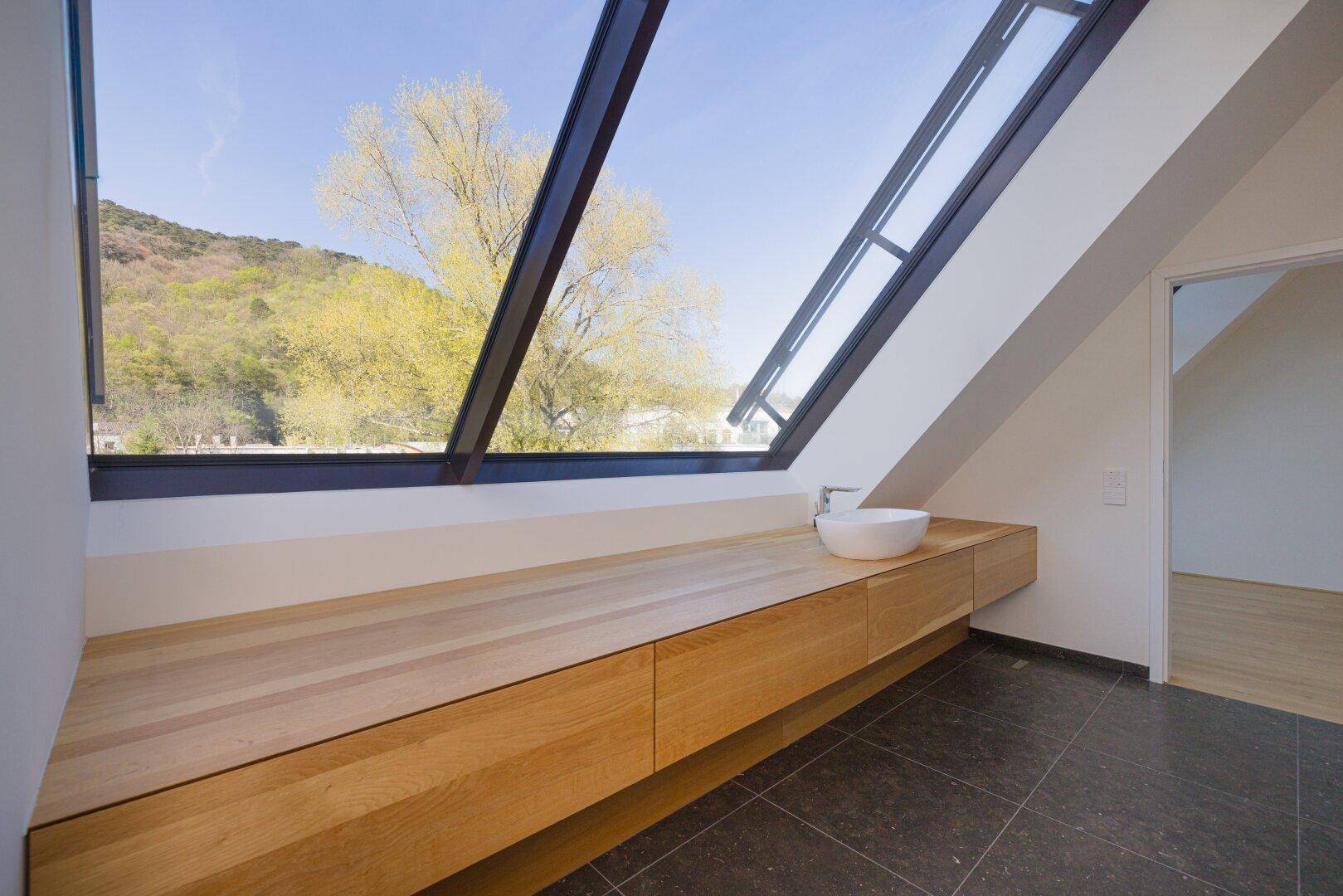 Modernes Badezimmer mit Holztresen, Aufsatzwaschbecken und großem Schrägfenster.