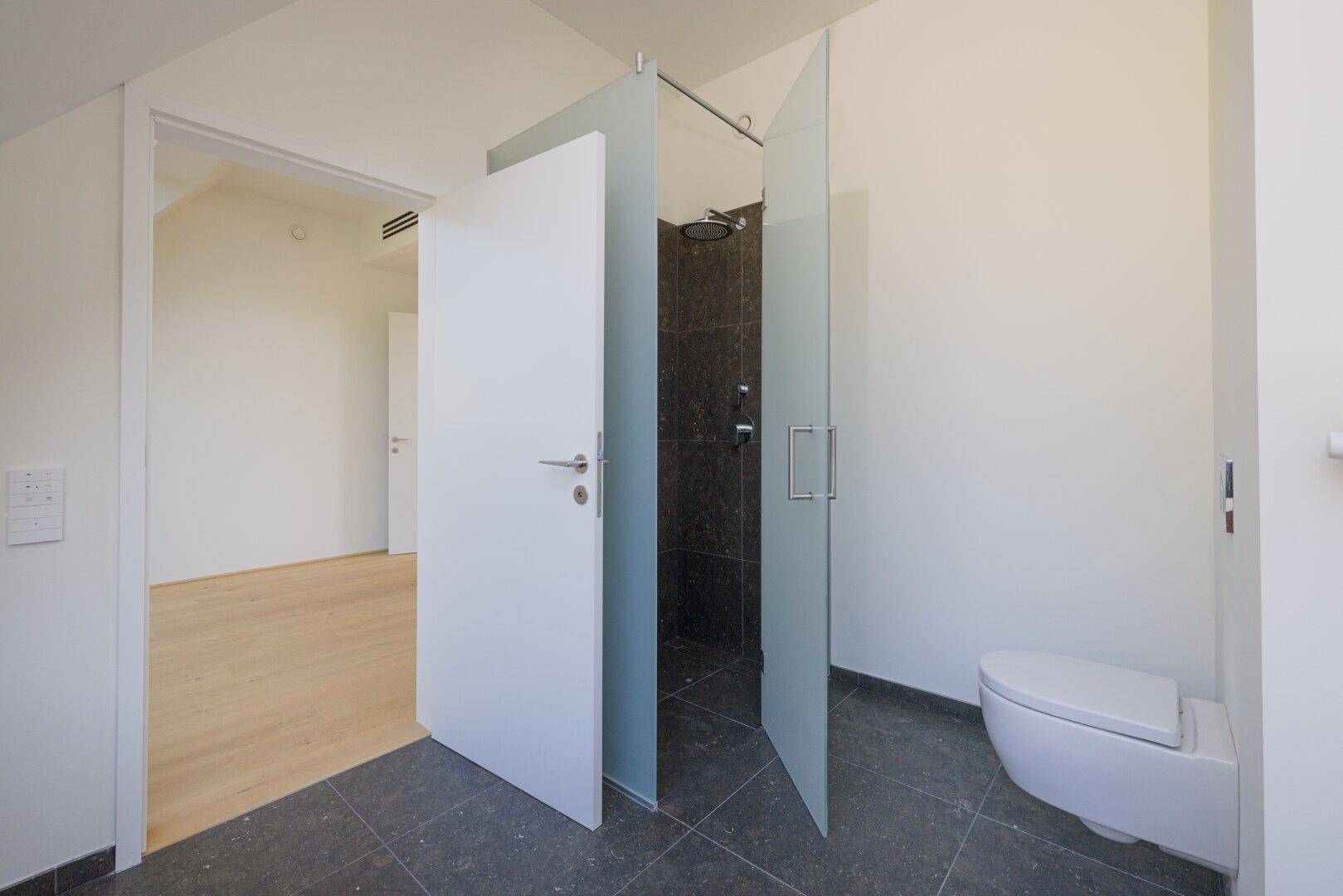 Zeitgemäßes Badezimmer mit ebenerdiger Dusche, Wand-WC und dunklen Fliesen.