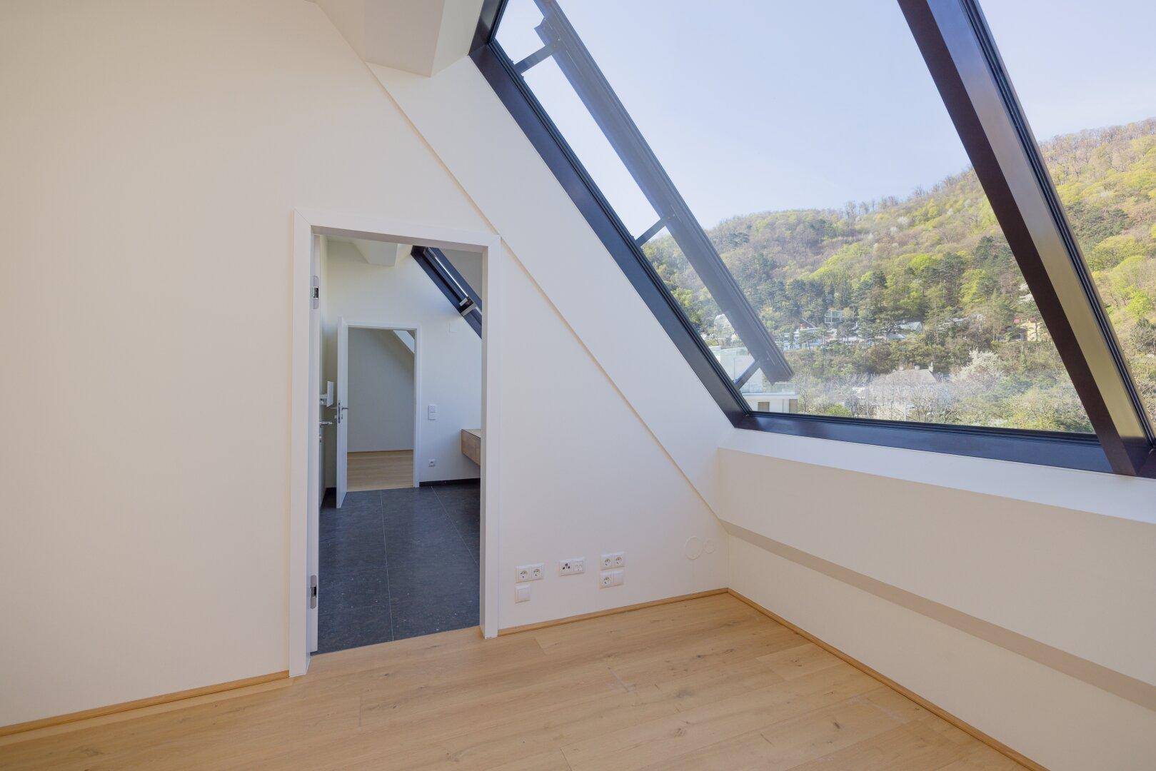 Schlafzimmer mit Holzboden, Schrägfenster und direktem Zugang zum Badezimmer.