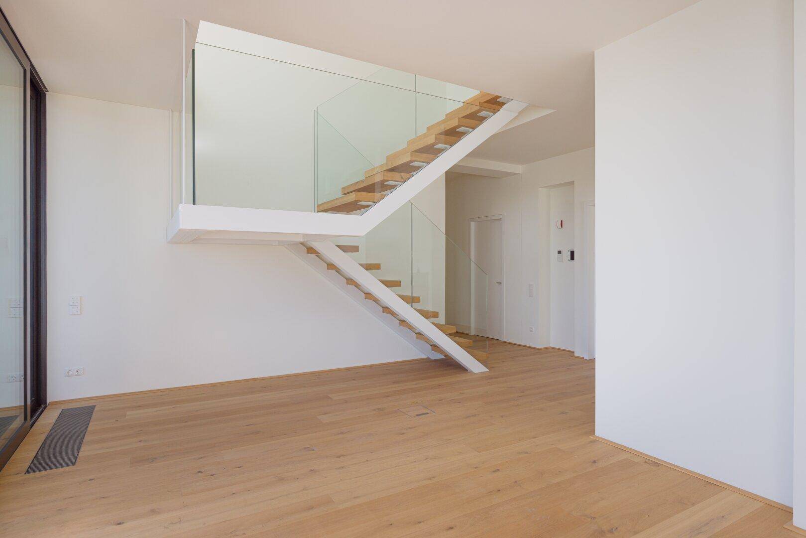 Elegante, freischwebende Holztreppe mit Glasgeländer in einem hellen Eingangsbereich.