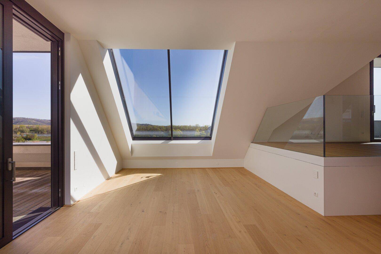 Geräumiger Dachgeschossraum mit großem Schrägfenster und weitem Blick auf die Umgebung.