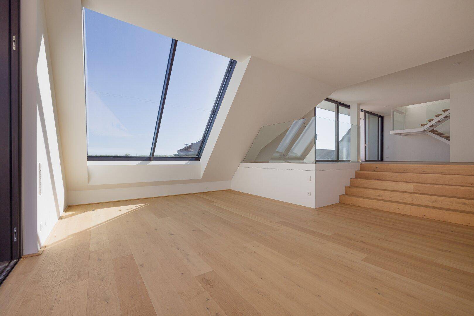 Offener Dachgeschossbereich mit Holzstufen, Schrägfenstern und viel natürlichem Licht.