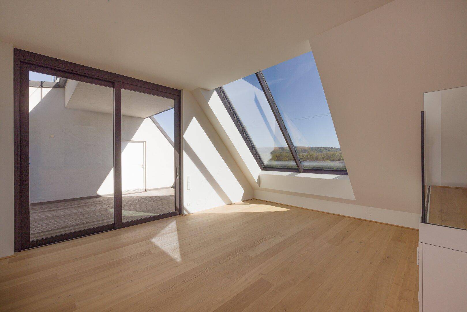 Lichtdurchfluteter Dachgeschossraum mit beeindruckendem Schrägfenster und Holzboden.