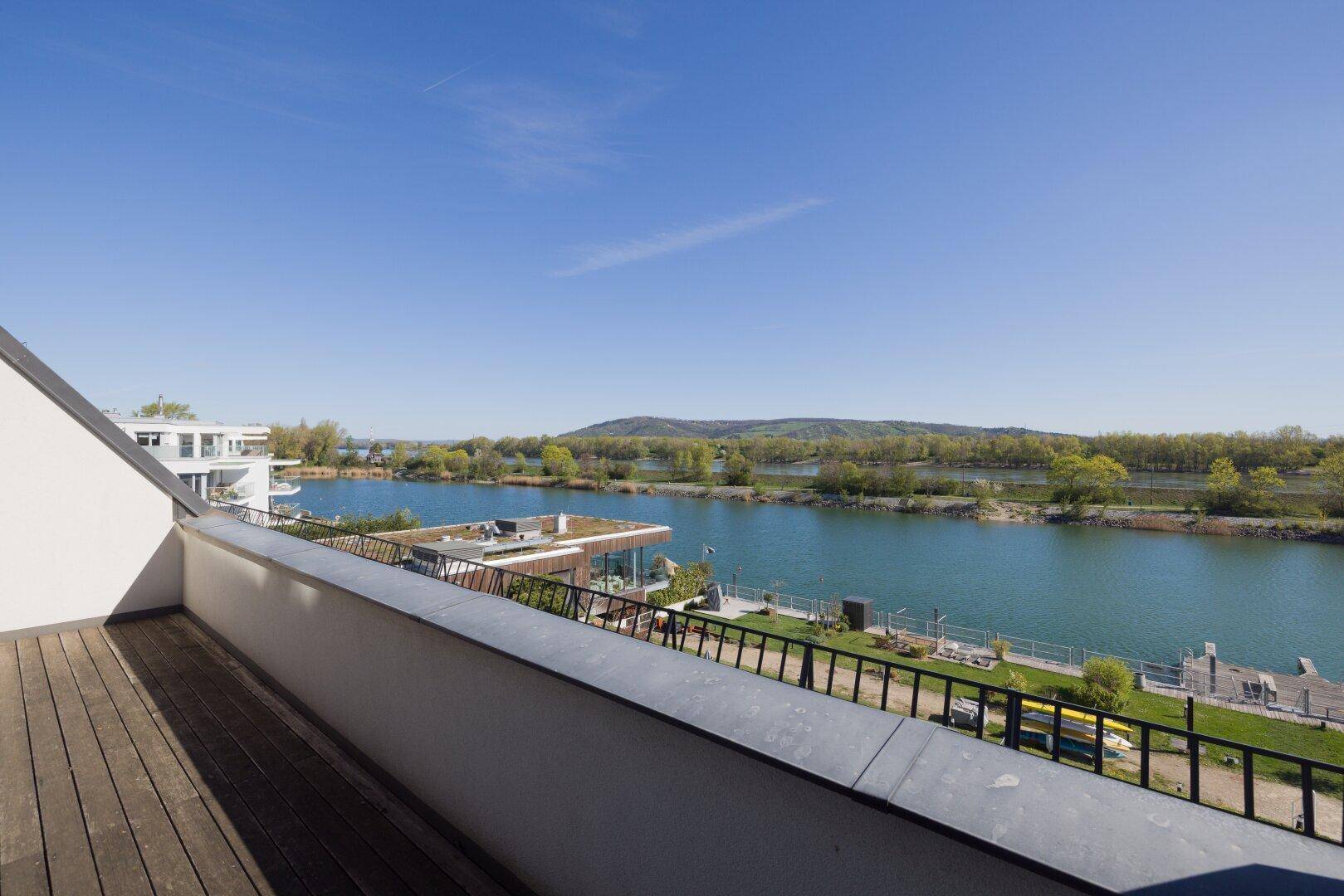 Geräumiger Balkon mit Holzboden und weitem Blick über den See und die umliegende Landschaft.