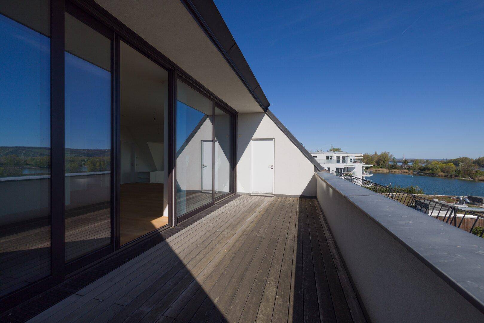 Langer Balkon mit Holzboden und weitem Blick auf den See und die grüne Umgebung.