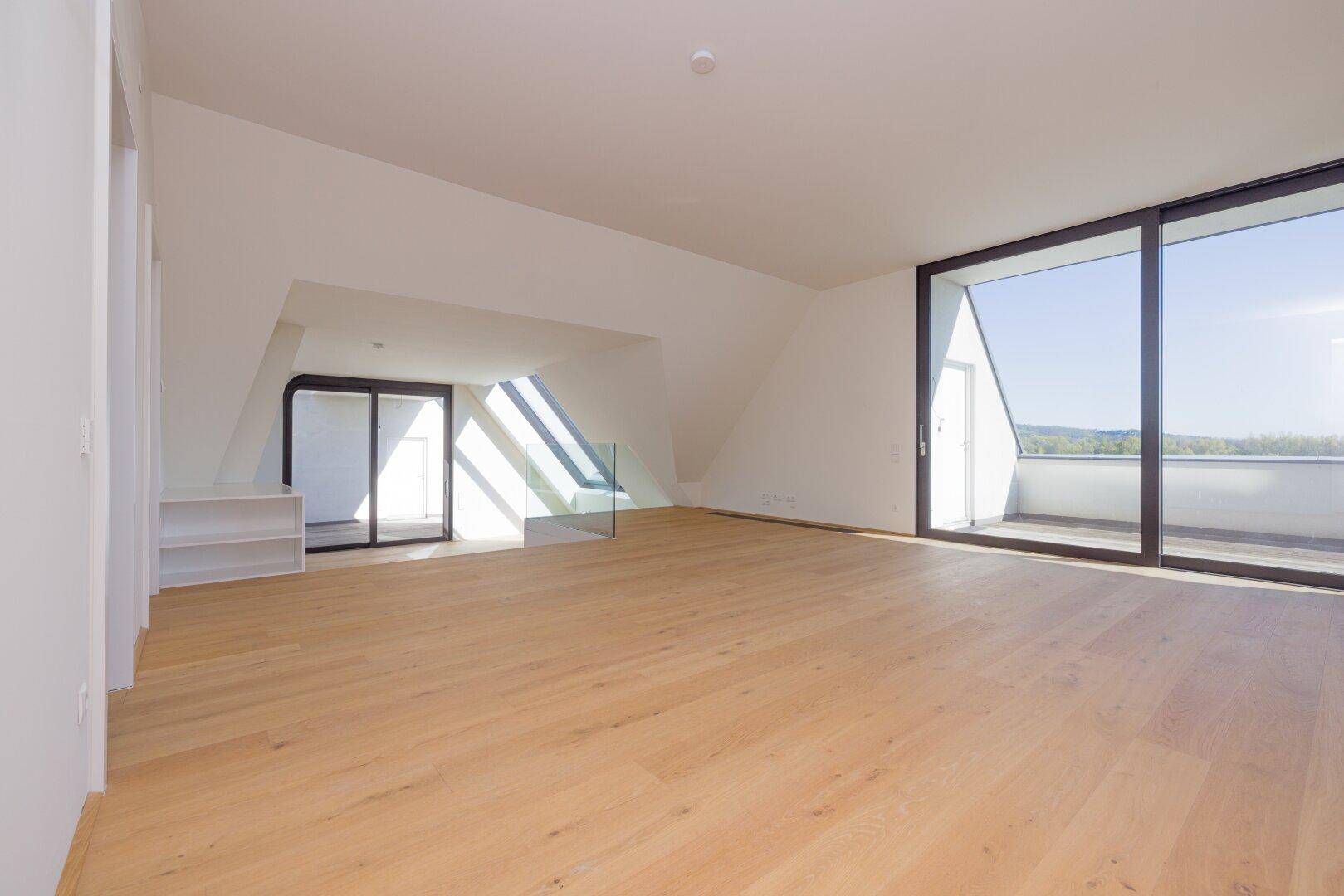 Heller Dachgeschossraum mit großen Fenstern und Zugang zu einem weiteren Balkon.
