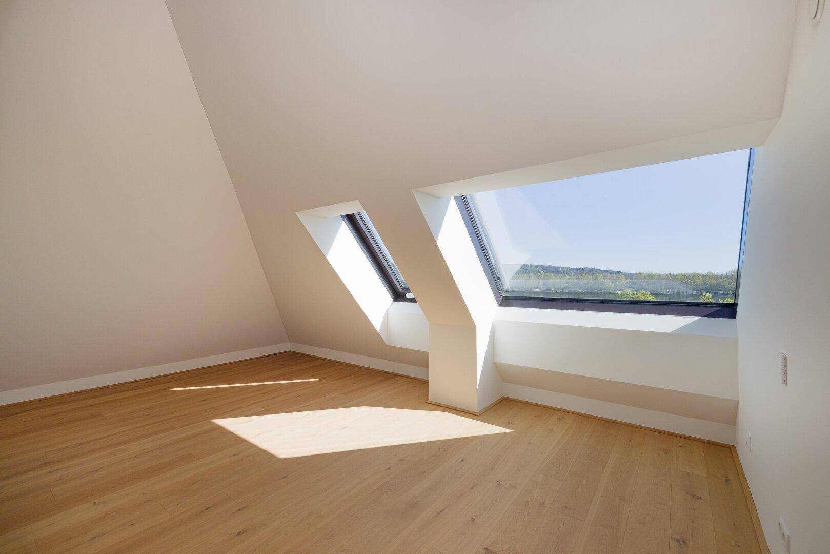 Lichtdurchfluteter Raum im Dachgeschoss mit Holzboden und weitem Ausblick.