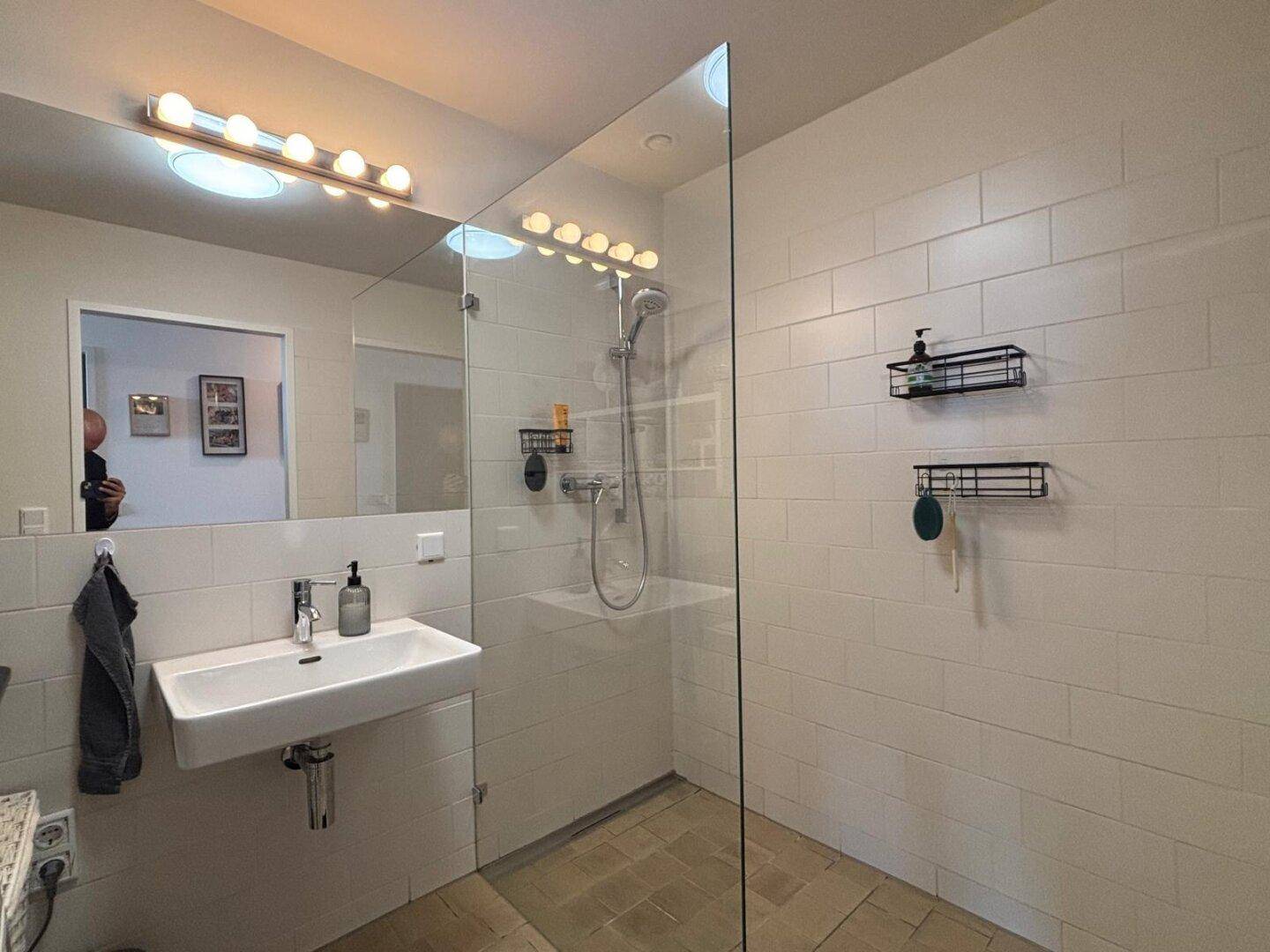 Helles Badezimmer mit ebenerdiger Dusche, modernem Waschbecken und großem Spiegel.