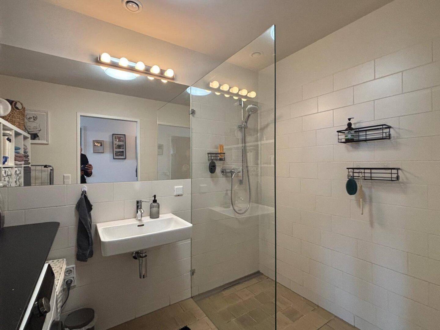 Funktionelles Badezimmer mit begehbarer Dusche, Waschbecken und integrierter Waschmaschine.