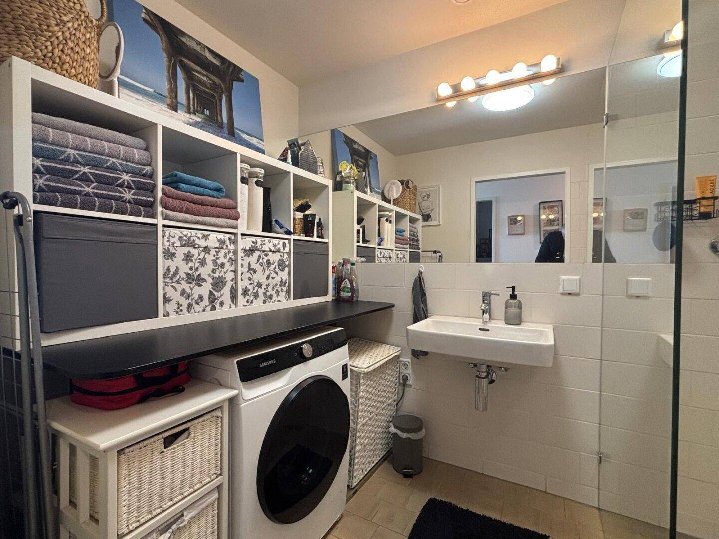 Modernes Badezimmer mit Waschmaschine, Waschbecken und großem Spiegel.