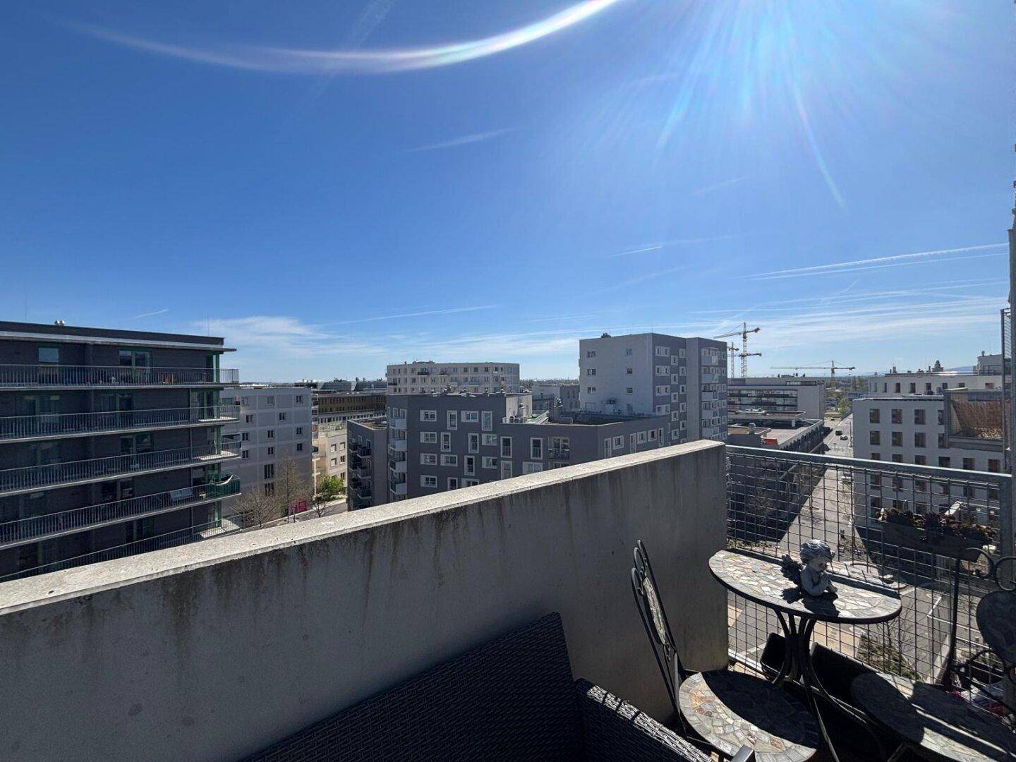 Weitläufiger Stadtblick von einem sonnigen Balkon mit klarem Himmel.