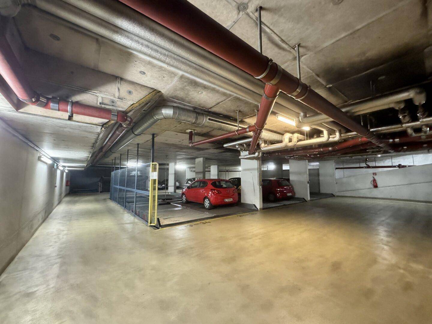 Bereich der Tiefgarage mit sichtbaren Rohrleitungen an der Decke und weiteren abgestellten Fahrzeugen.