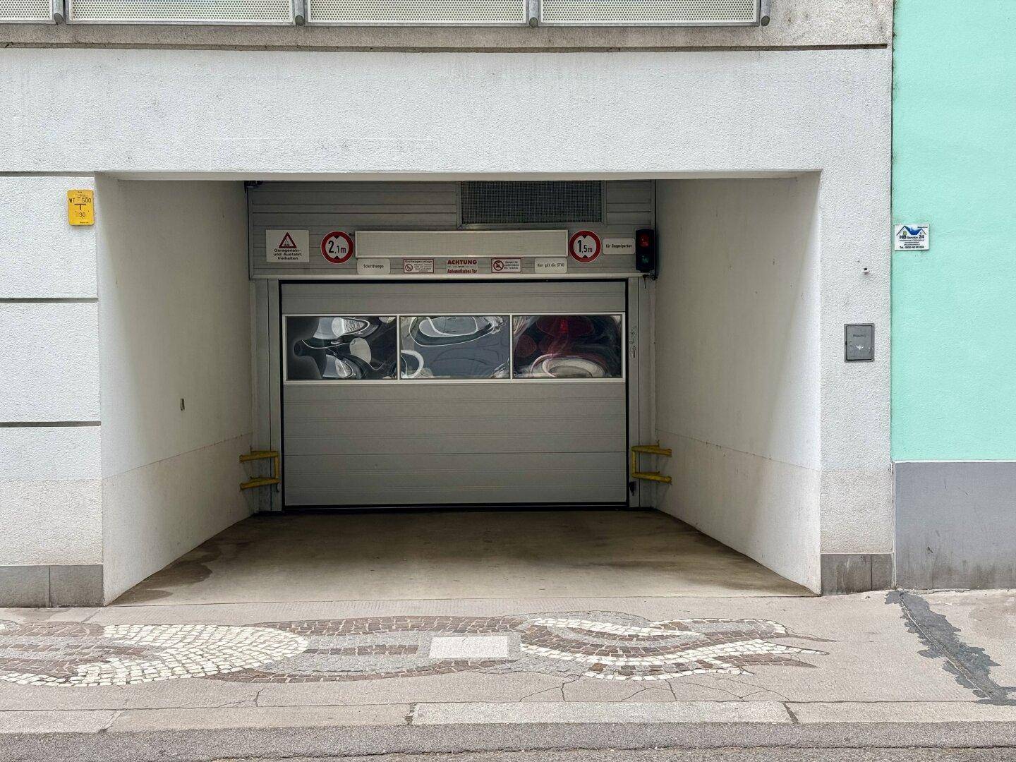 Eingang zu einer Tiefgarage mit geschlossenem Tor und sichtbaren Höhenbegrenzungen für Fahrzeuge.