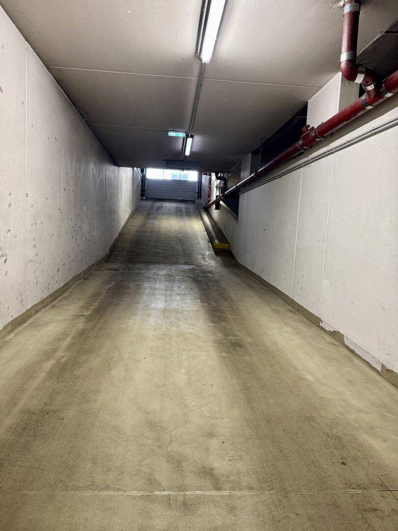 Lange, abfallende Betonrampe führt in die Tiefe einer unterirdischen Parkgarage.