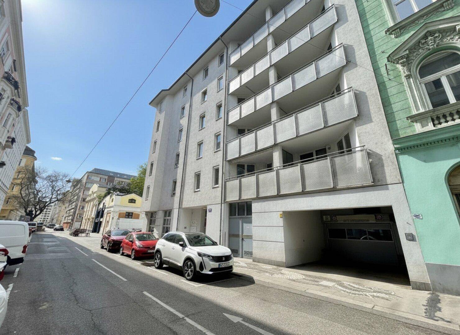 Modernes Mehrfamilienhaus mit mehreren Balkonen und einer Tiefgarageneinfahrt an einer städtischen Straße.