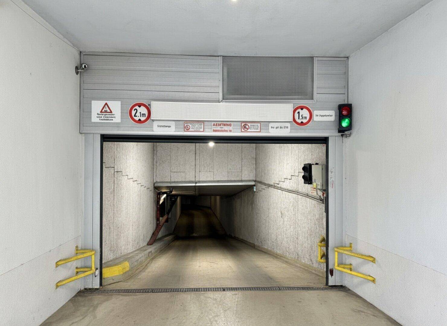 Einfahrt zu einer Tiefgarage mit Rampe, Ampel und Höhenbegrenzungen für die Zufahrt.