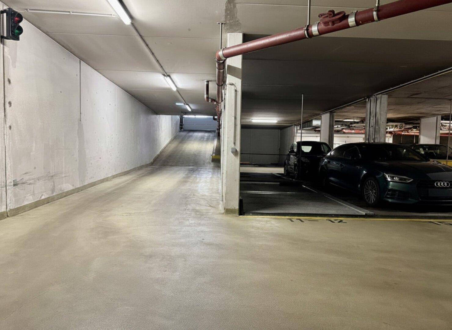 Unterer Bereich der Tiefgaragenrampe, der in den Parkbereich mit abgestellten Fahrzeugen übergeht.