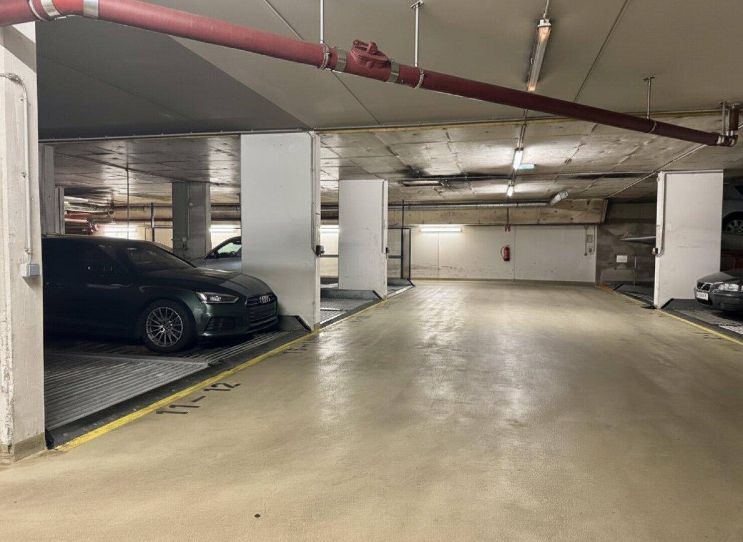 Innenansicht einer Tiefgarage mit mehreren Parkplätzen und hydraulischen Parksystemen für Fahrzeuge.