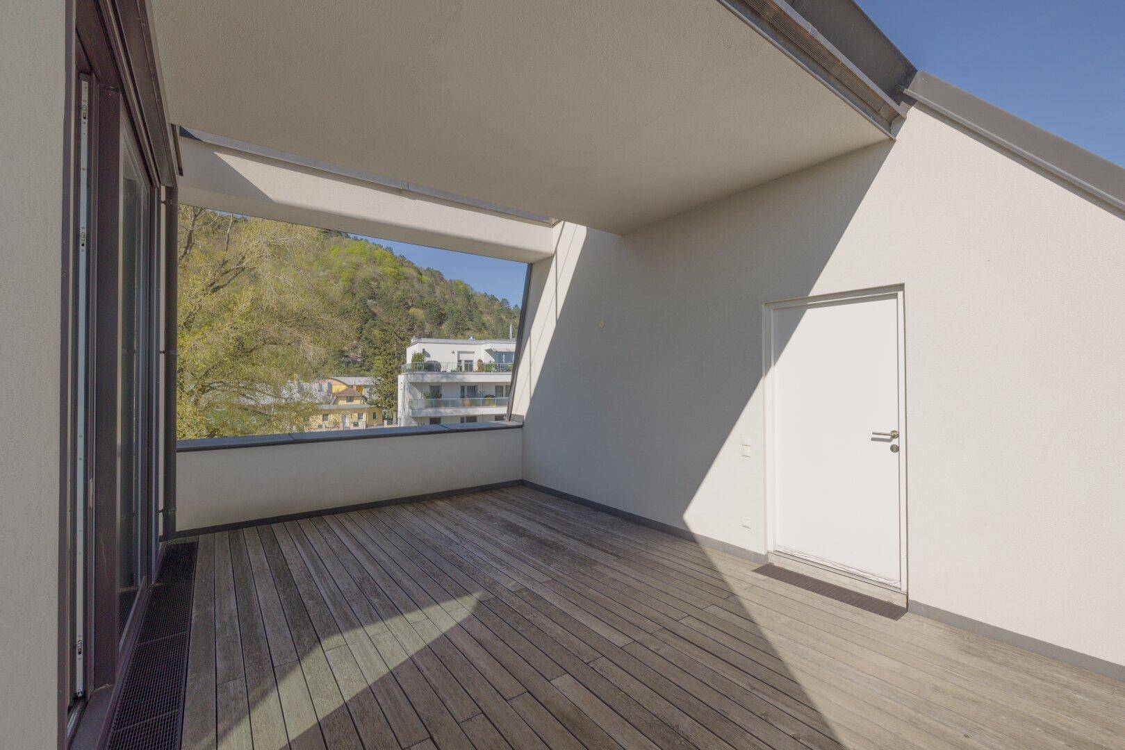 Überdachter Balkon mit Holzboden und Blick auf die umliegende Bebauung und Natur.