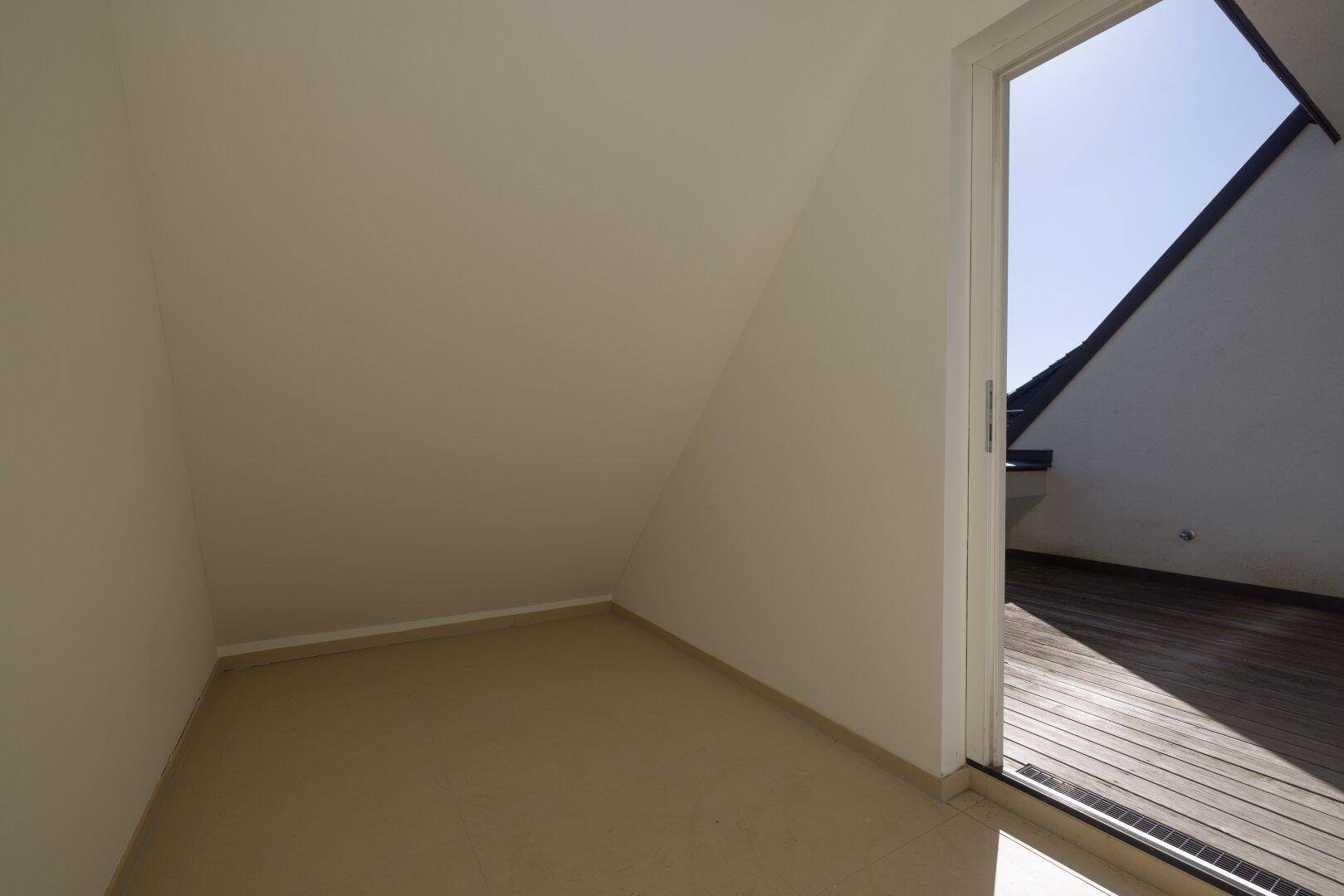 Kleiner, leerer Raum mit schrägen Wänden und Zugang zu einem Außenbereich.