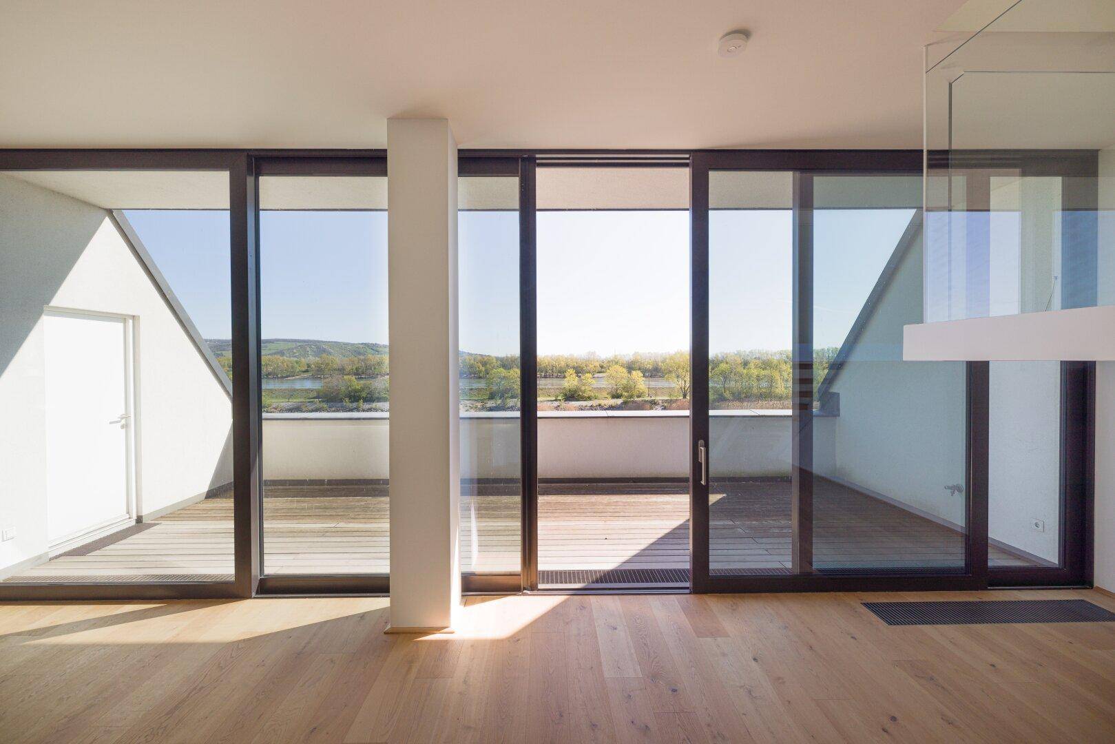 Heller, leerer Raum mit großen Schiebetüren, die auf einen Balkon mit Seeblick führen.