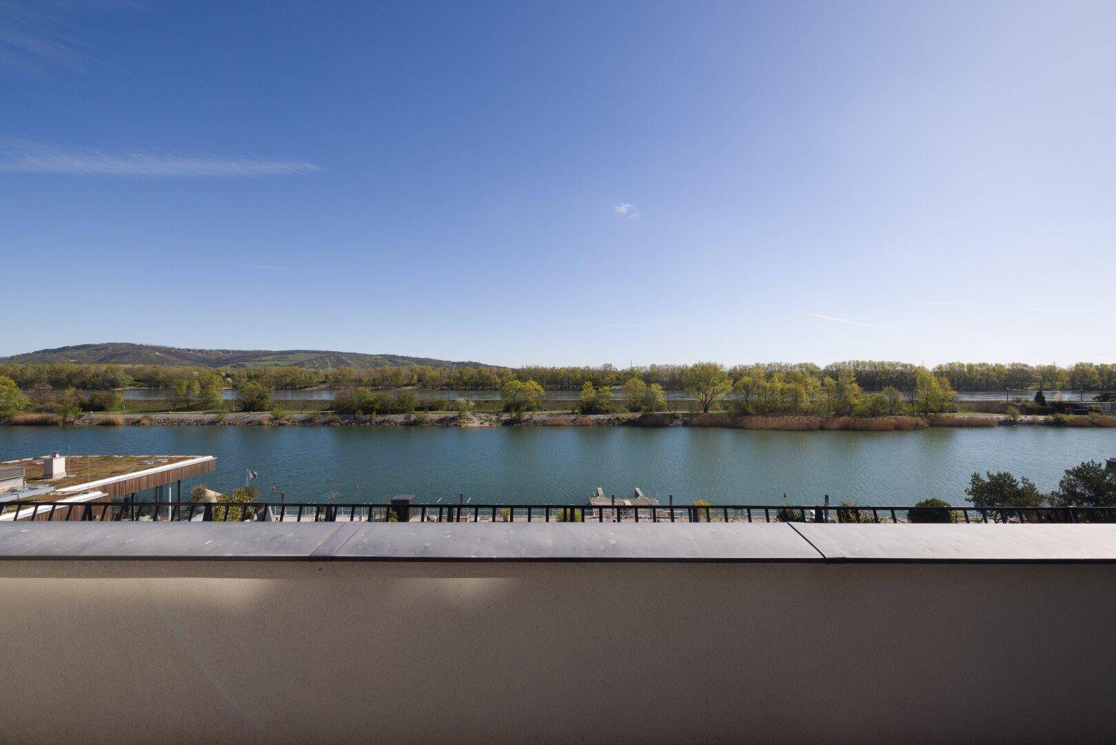 Panoramablick vom Balkon auf den ruhigen See und die bewaldeten Hügel in der Ferne.