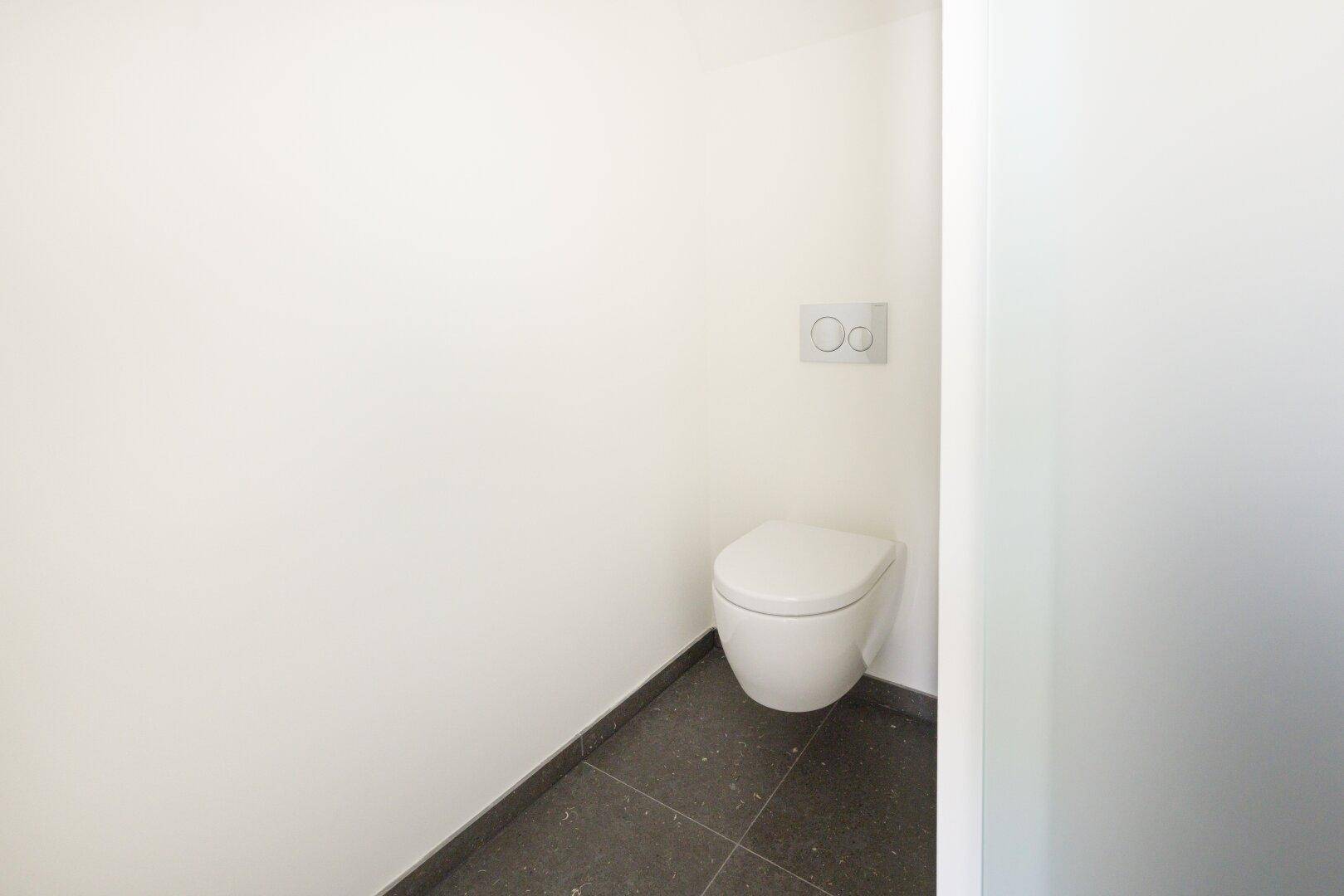 Modernes Gäste-WC mit wandhängender Toilette und dunklen Bodenfliesen.