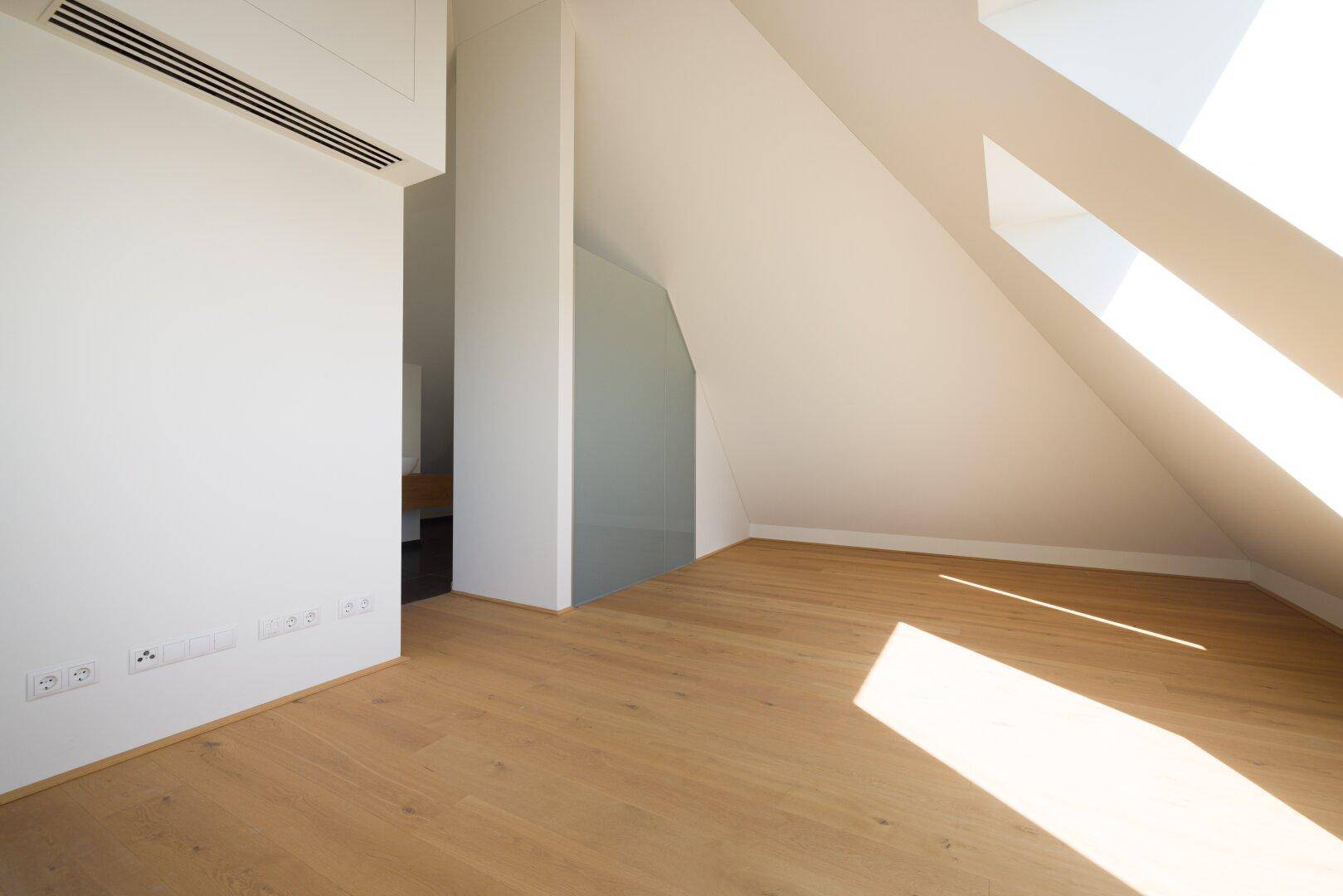 Heller Dachgeschossraum mit Holzboden, schrägen Wänden und viel Tageslicht.