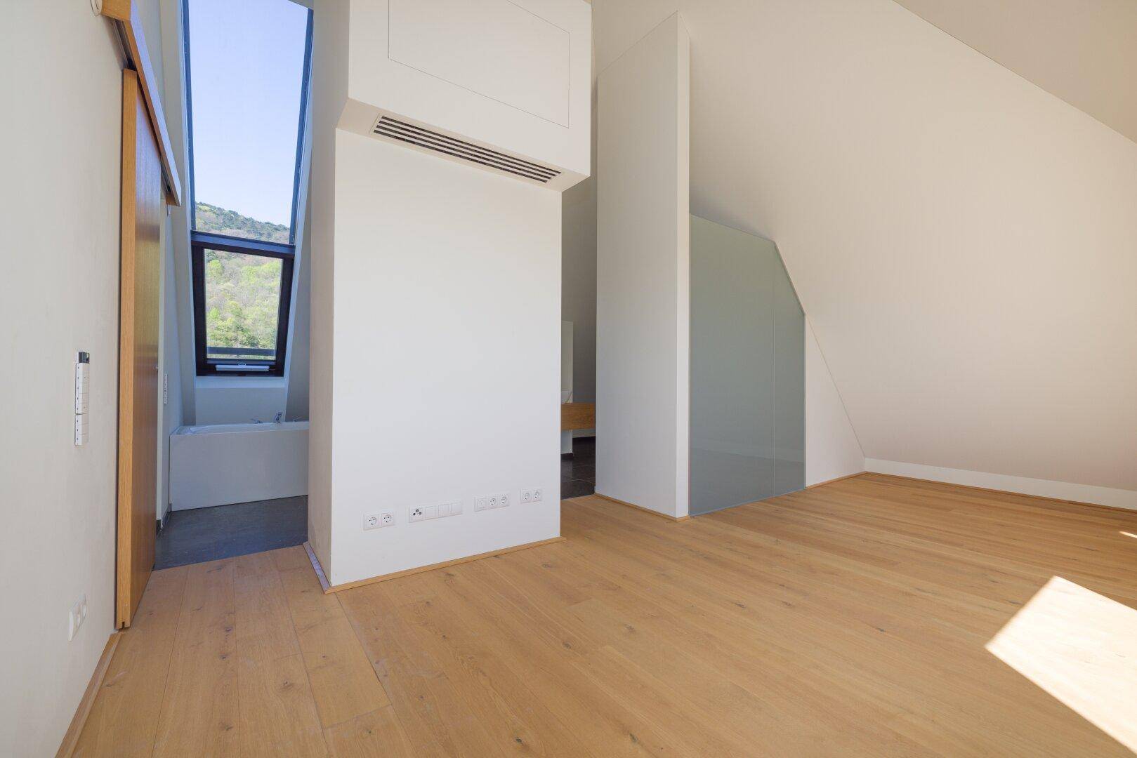 Geräumiger Dachgeschossraum mit Holzboden und Zugang zu einem modernen Badezimmer.