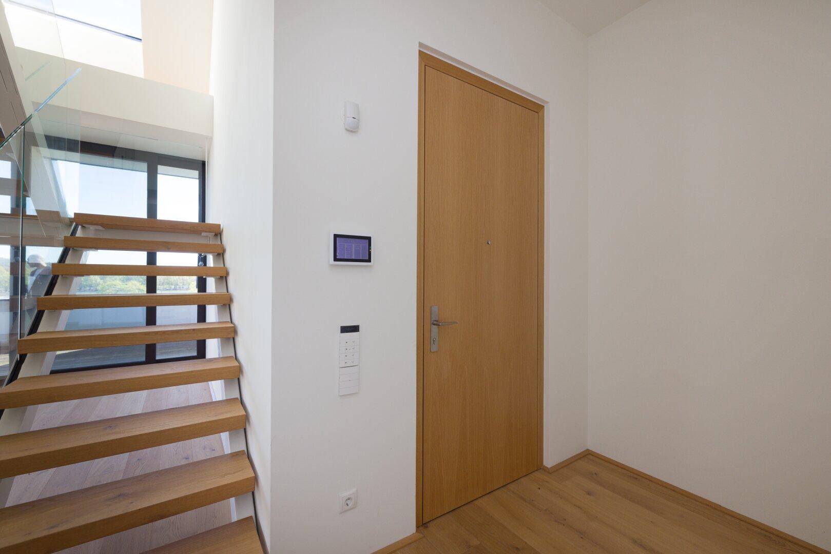 Moderner Eingangsbereich mit Holztreppe und heller Holztür.