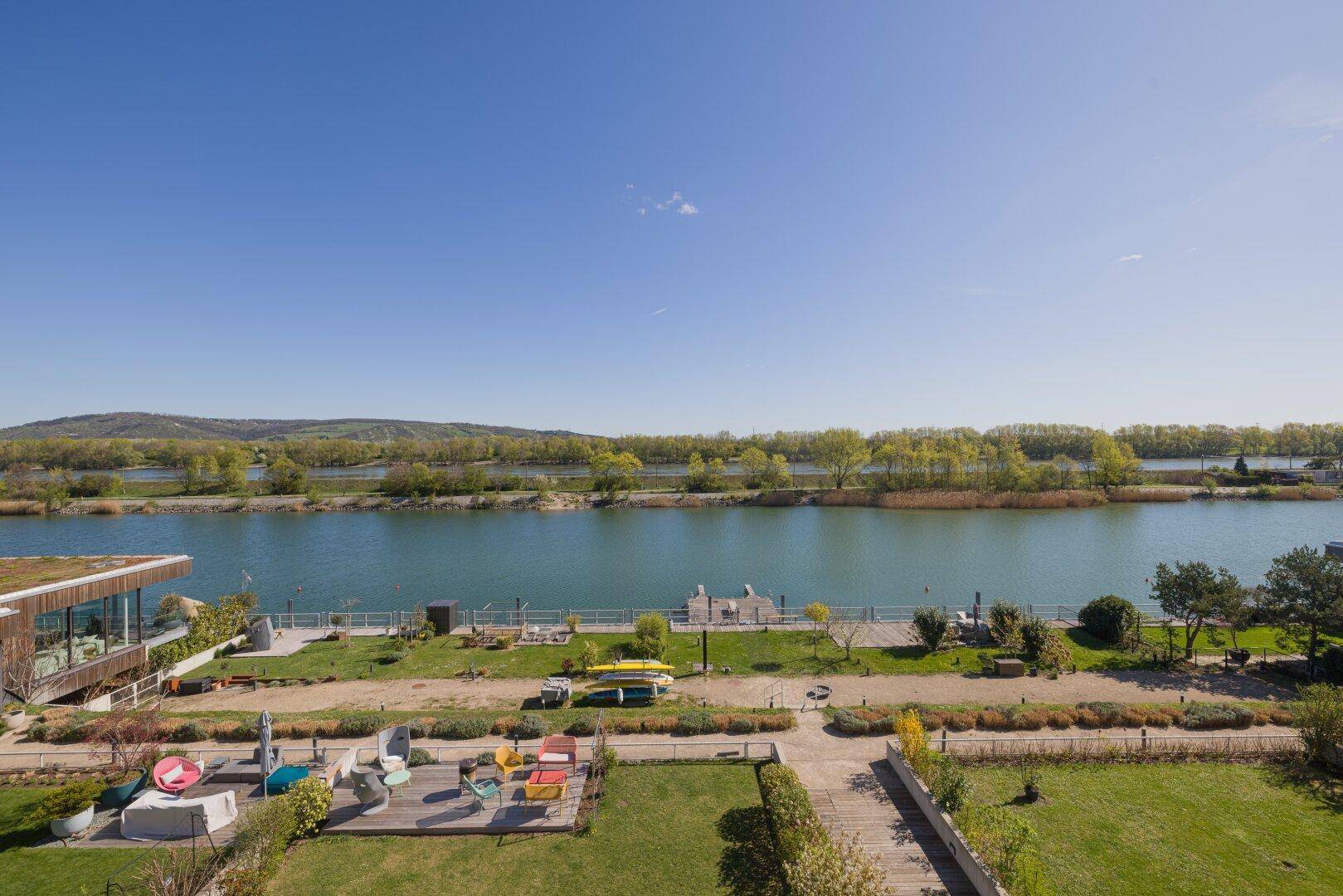 Weitläufige Gartenanlage mit verschiedenen Sitzbereichen und Blick auf den See.