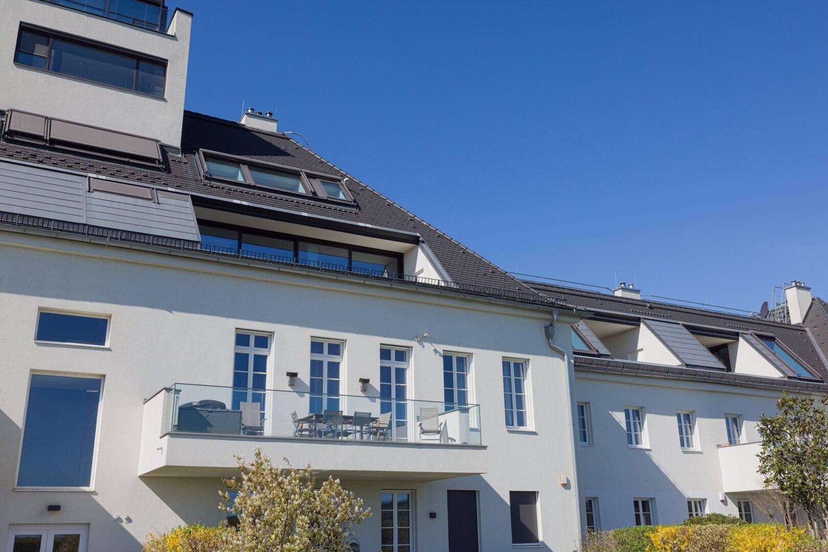 Moderne Wohnanlage mit weißer Fassade, Balkonen und großen Dachfenstern.