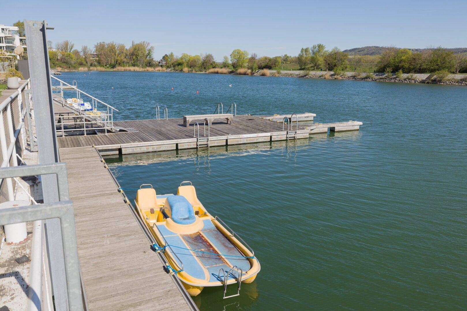 Anlegestelle mit Tretboot und Holzsteg am ruhigen Seeufer.