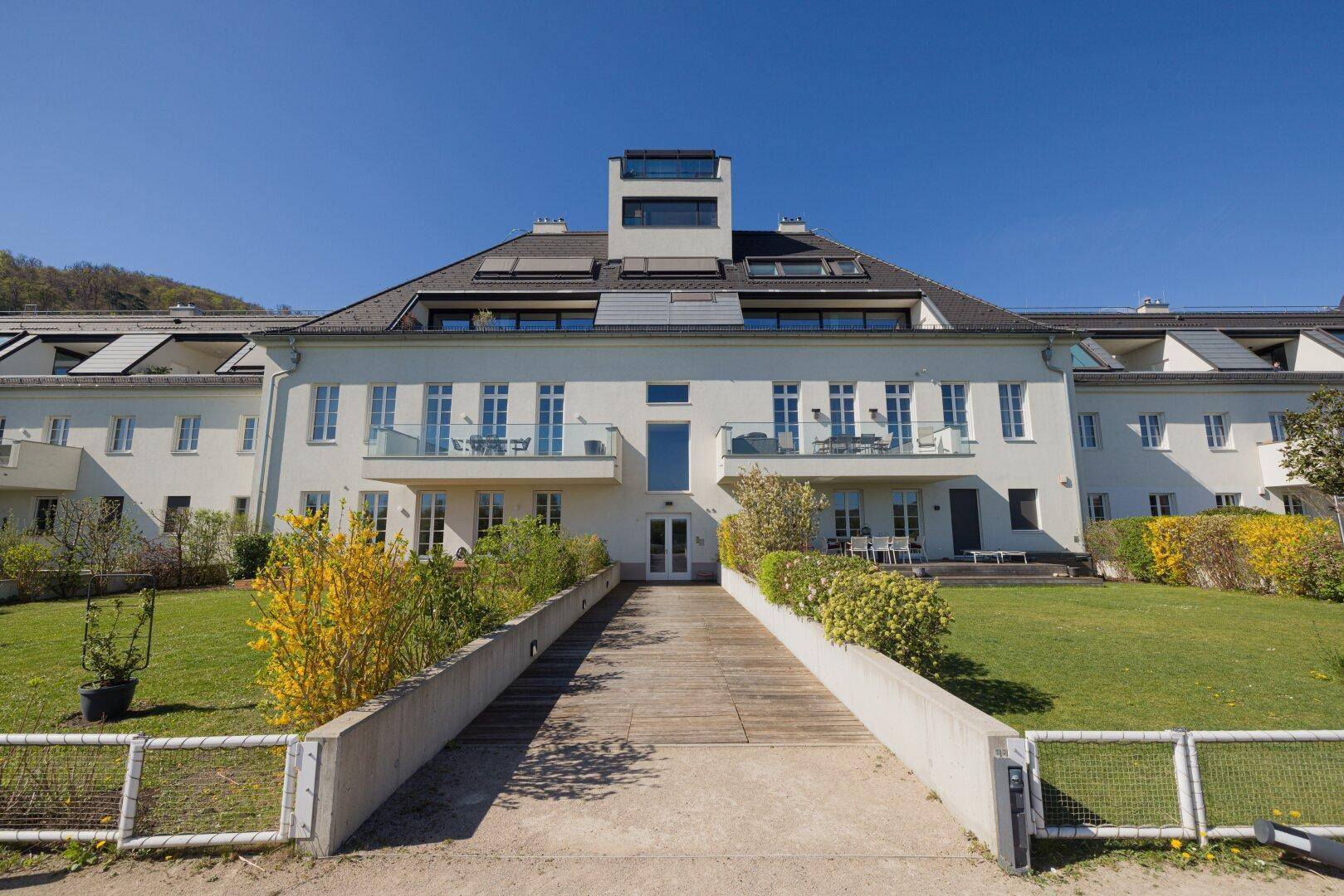 Elegante Wohnanlage mit weißer Fassade, Balkonen und gepflegter Grünfläche.