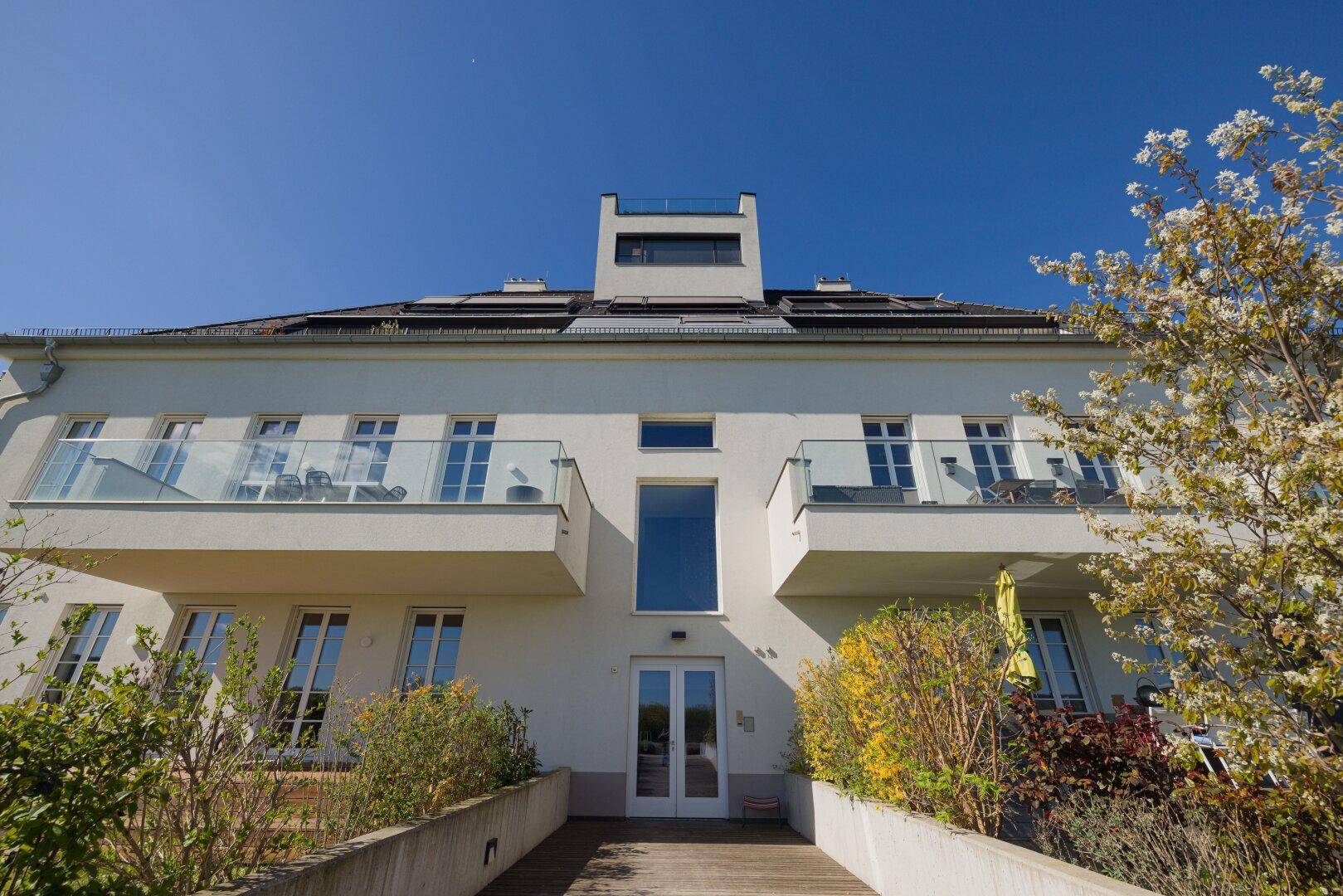 Moderne Wohnanlage mit weißer Fassade, Balkonen und großen Fenstern unter blauem Himmel.