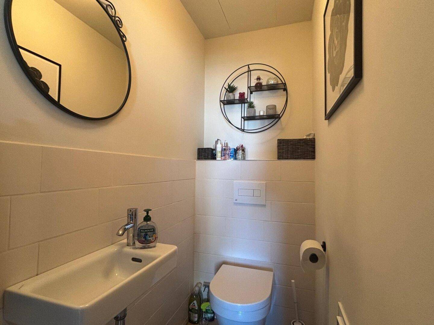 Modernes Gäste-WC mit wandhängender Toilette, kleinem Waschbecken und Spiegel.