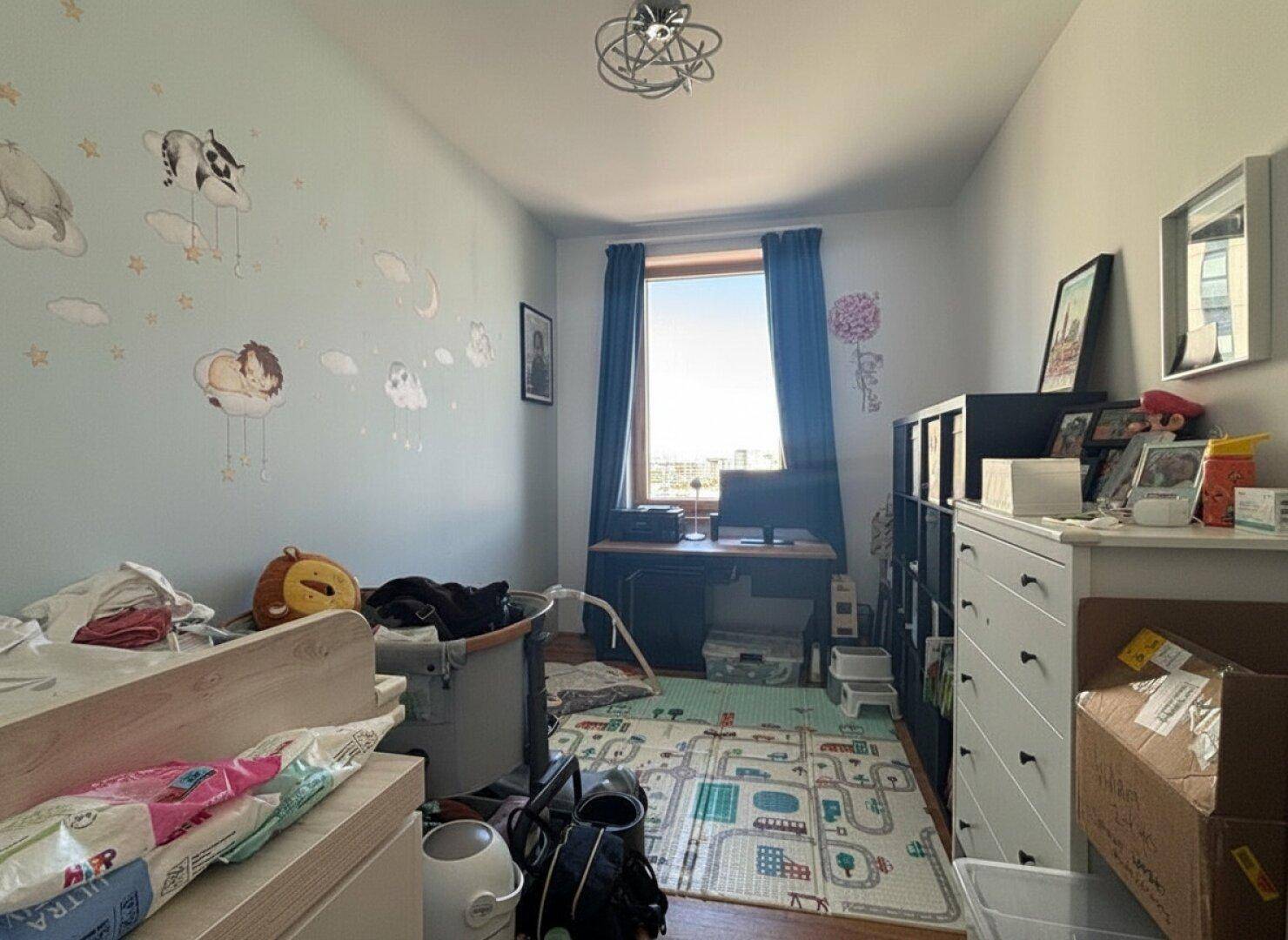 Kinderzimmer mit Schreibtisch, Spielteppich und Blick aus dem Fenster.