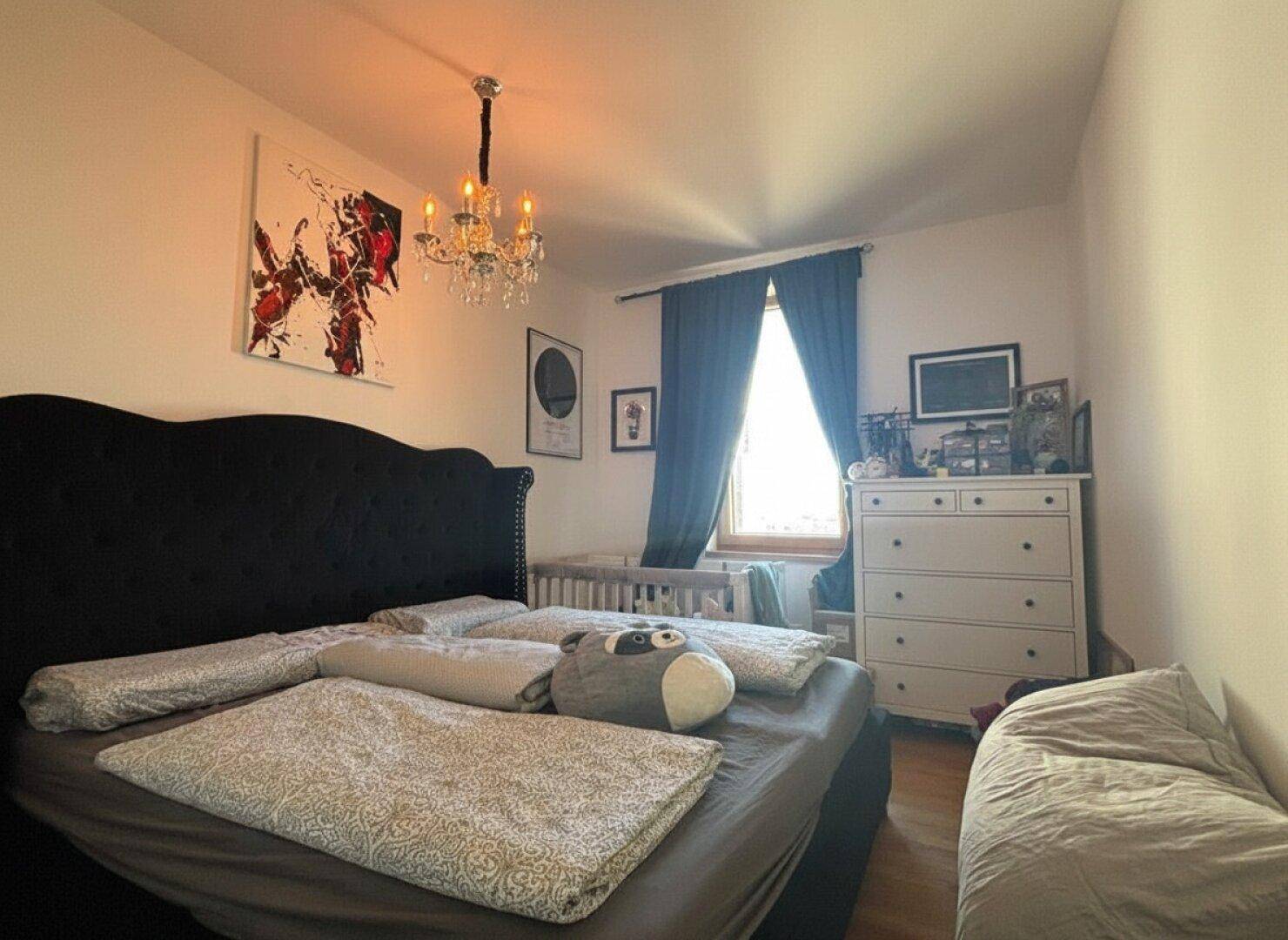 Schlafzimmer mit großem Bett, Babybett und Kronleuchter für eine gemütliche Atmosphäre.