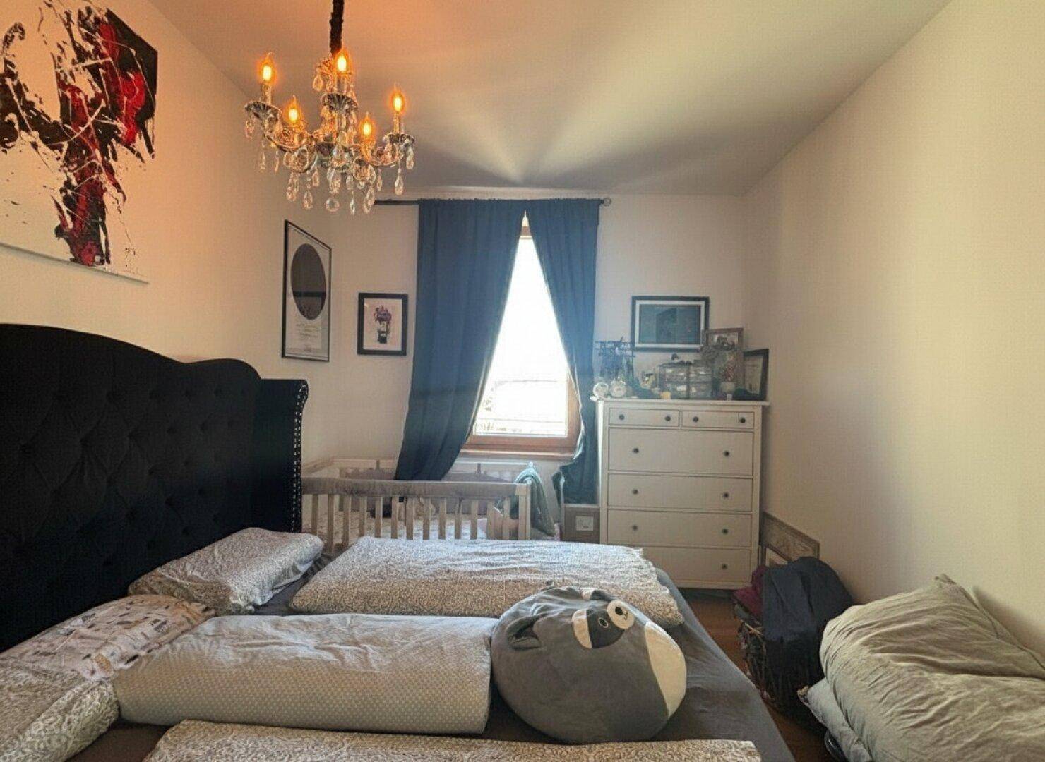 Gemütliches Schlafzimmer mit Doppelbett, Babybett und elegantem Kronleuchter.