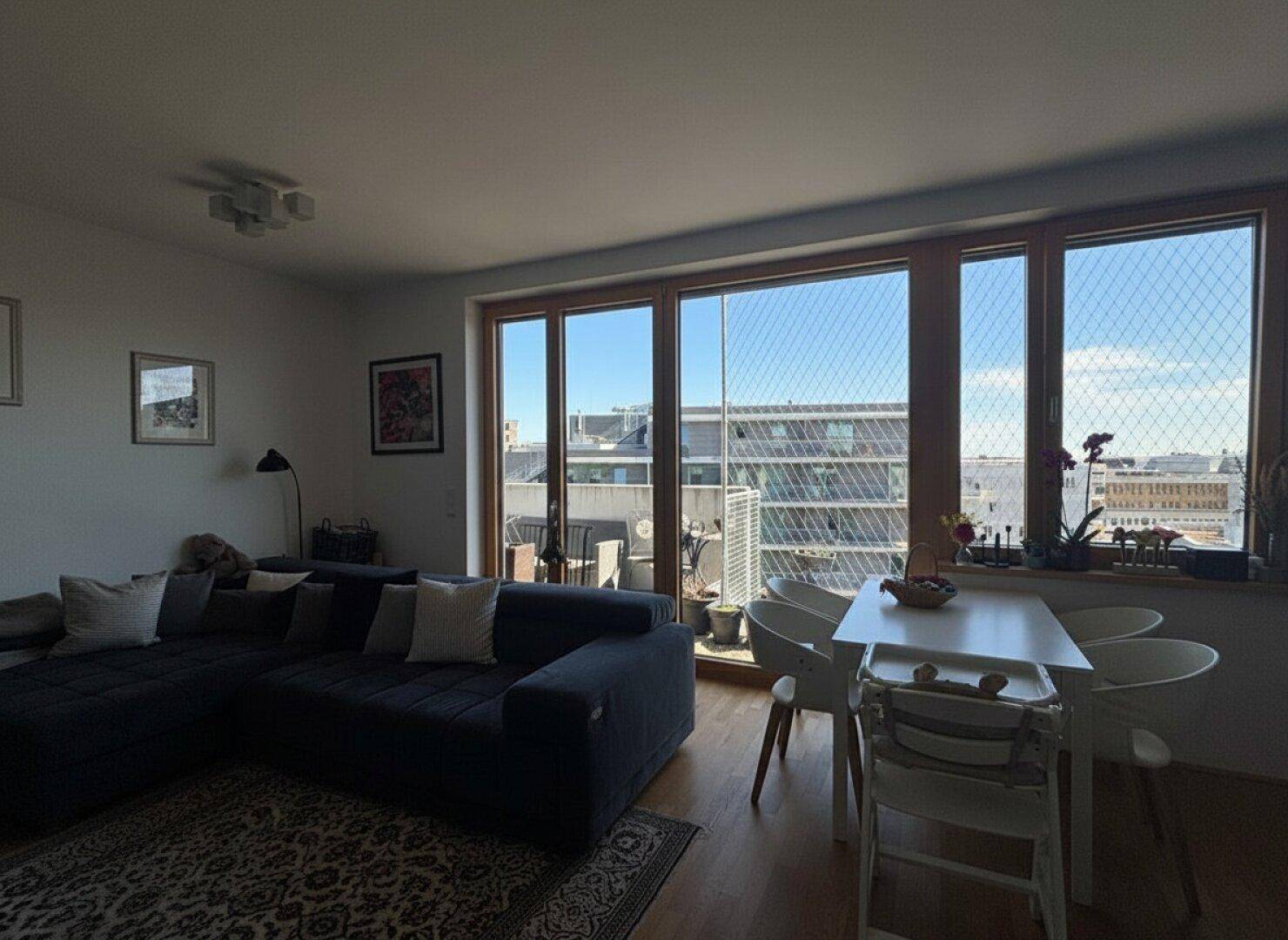 Lichtdurchfluteter Wohn- und Essbereich mit bequemer Couch und Blick auf die Stadt.
