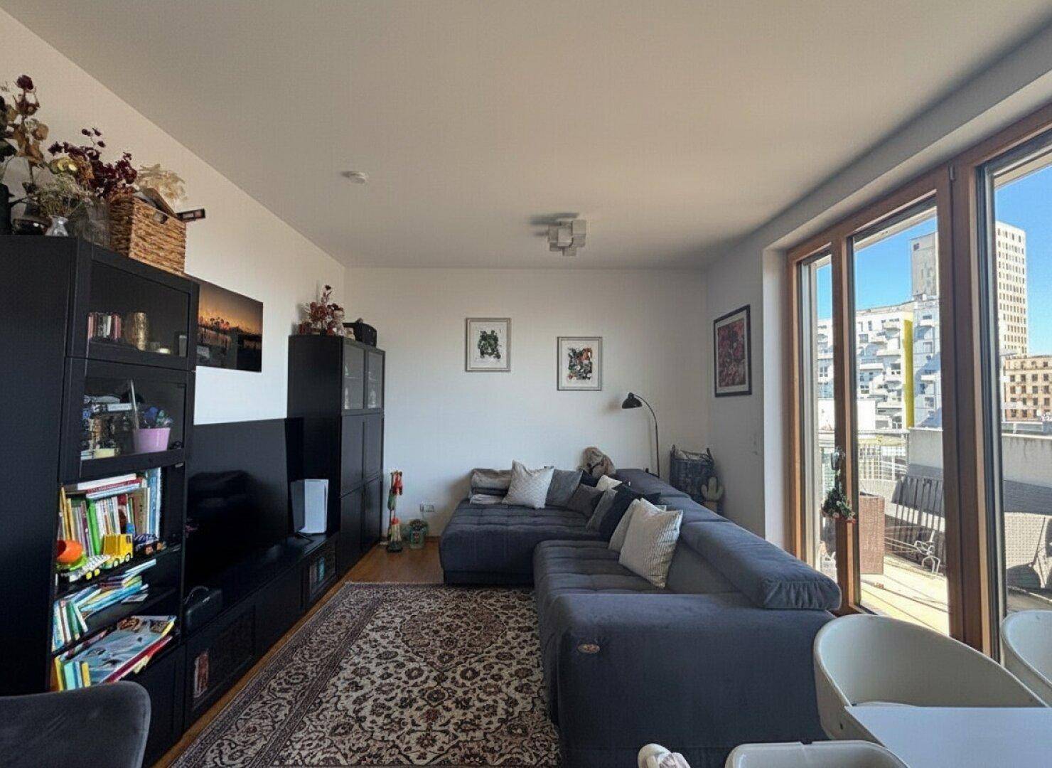Gemütliches Wohnzimmer mit großem Ecksofa, Teppich und Blick auf die Stadt.